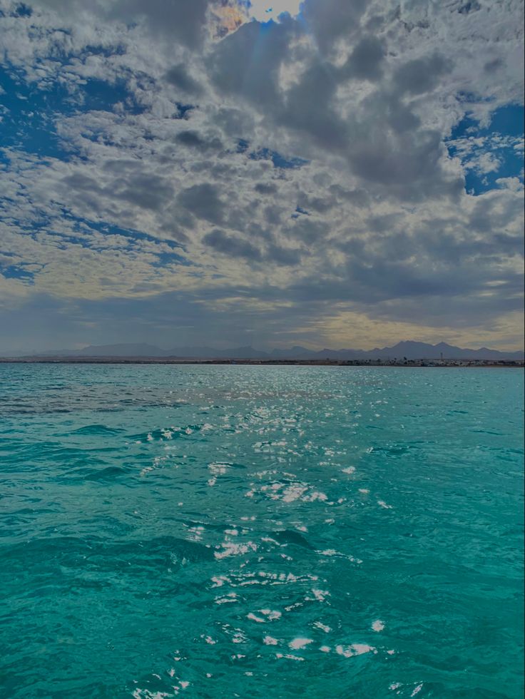 the sky is filled with clouds and blue water as seen from a boat in the ocean