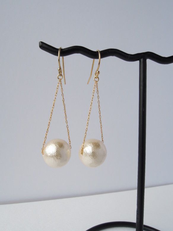 two white pearls are hanging from gold chain earrings on a black hook - link stand