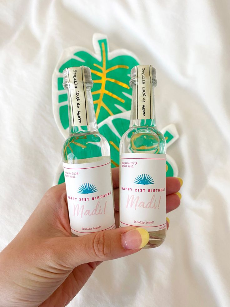 two bottles of alcohol sitting on top of a white bed next to a green and yellow sticker