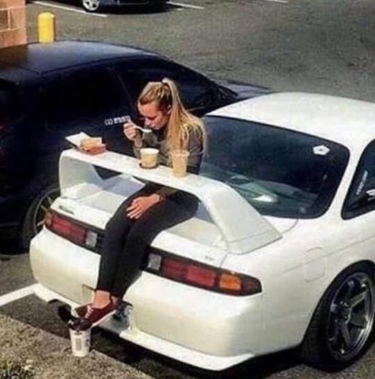 a woman sitting on top of a white car in a parking lot next to other cars