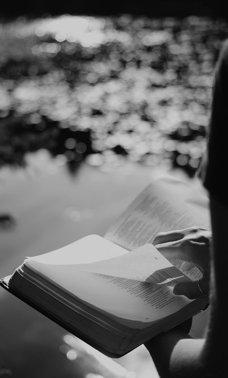 a person is reading a book by the water's edge while holding it in their hands