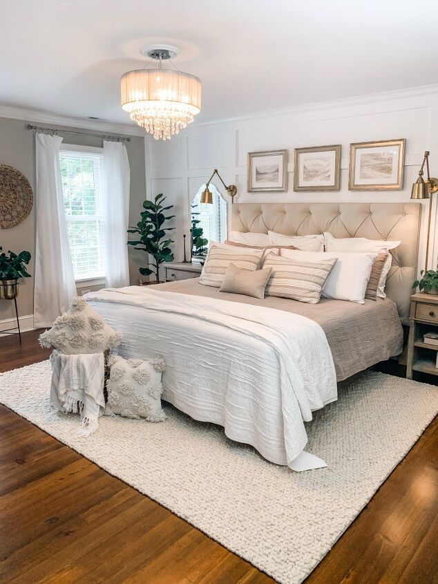 a bedroom with white walls and wood flooring has a chandelier above the bed