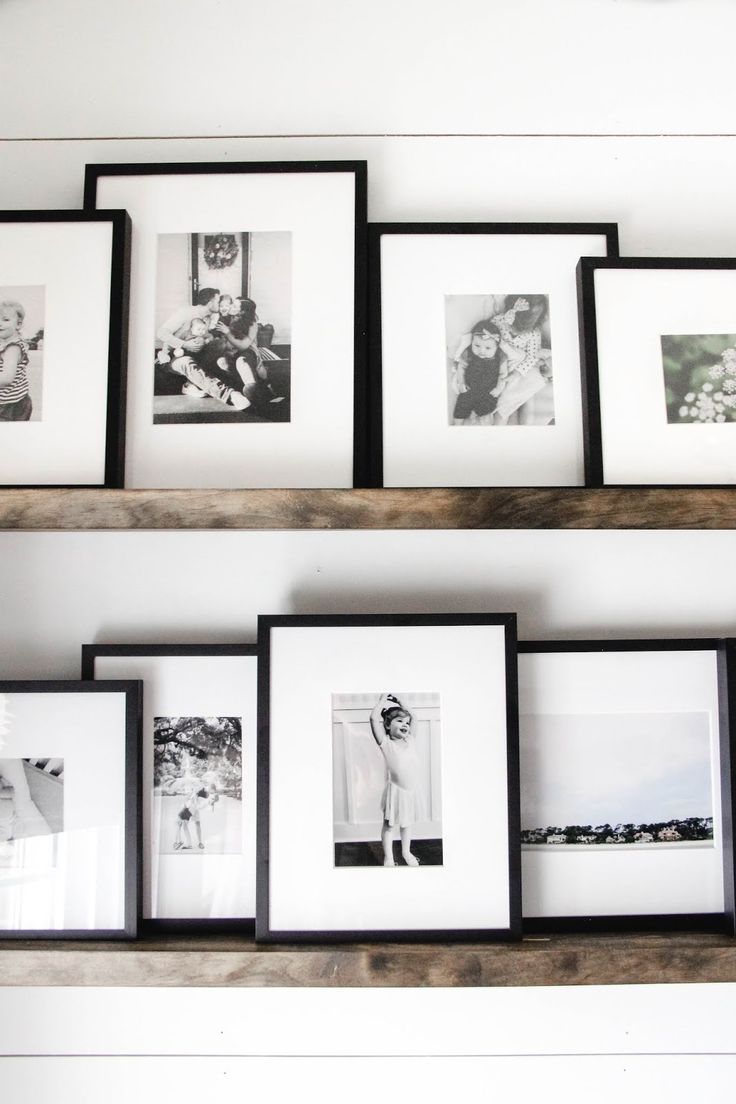 black and white photos are hanging on the wall above shelves with frames in them,