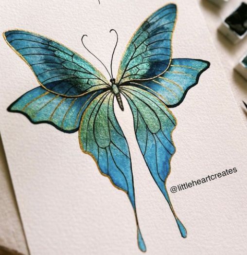 a blue and green butterfly is on top of a white card next to some watercolor pencils