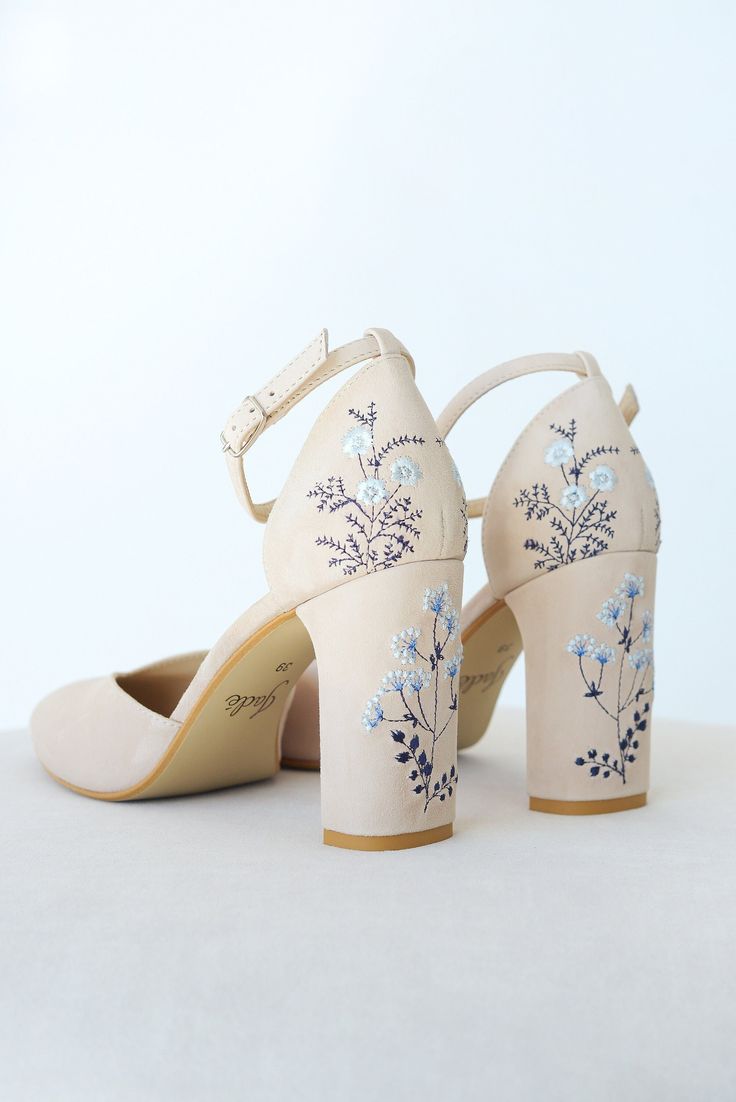 a pair of white shoes with blue flowers painted on the side and heels in front