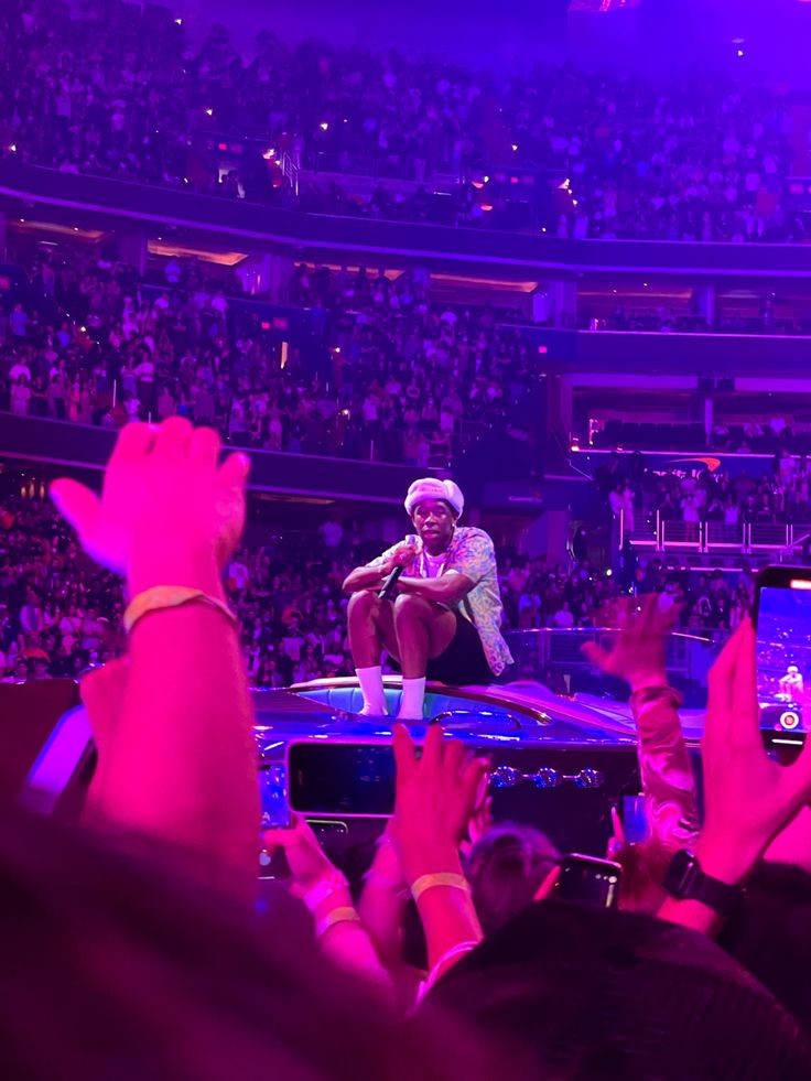 a man sitting on top of a car in front of a crowd at a concert