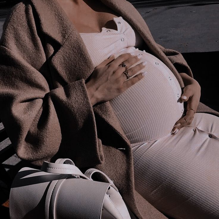 a pregnant woman sitting on a bench with her hand on her stomach and wearing a coat