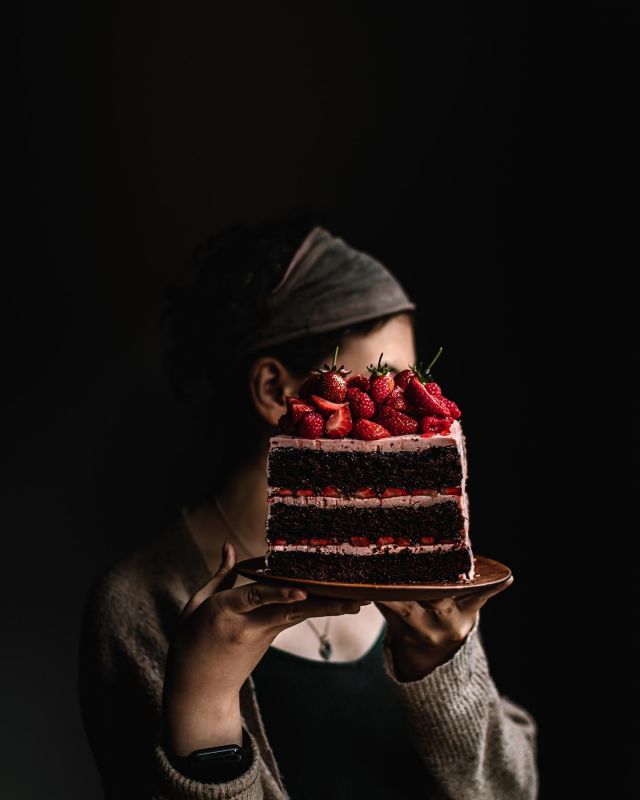 a woman holding a piece of cake with strawberries on top in front of her face