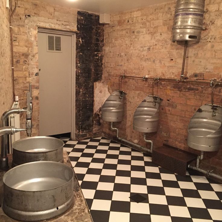 a bathroom with three urinals and a checkered floor in front of a brick wall