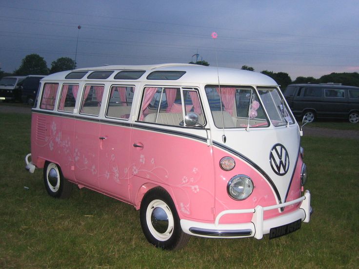 a pink and white vw bus parked on top of a grass covered field