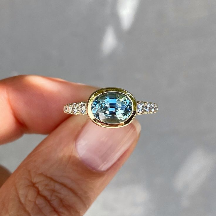 a woman's hand holding a ring with a blue topazte and diamond band