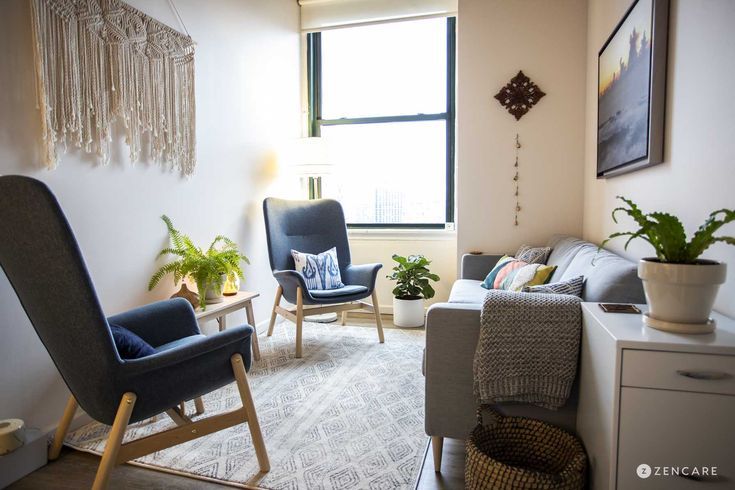 a living room with two chairs and a rug in front of a window that has plants on it