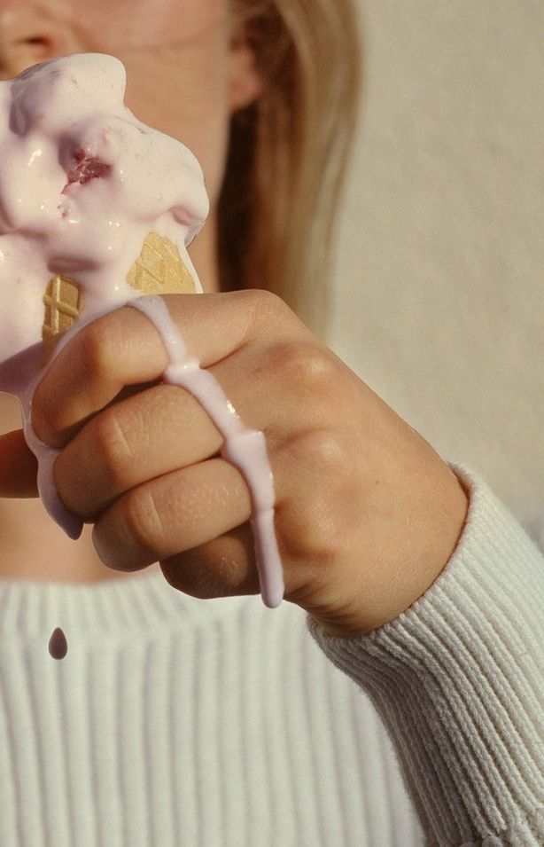 a woman holding up a piece of food with icing on it's fingers