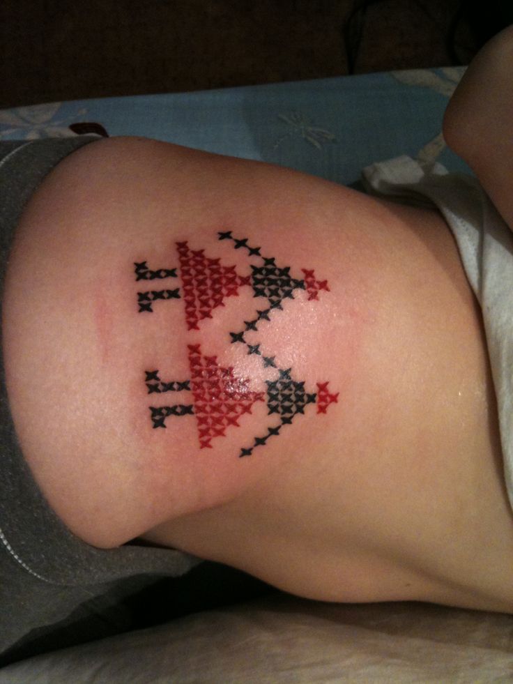 a cross stitch tattoo on the back of a woman's leg, with red and black crosses