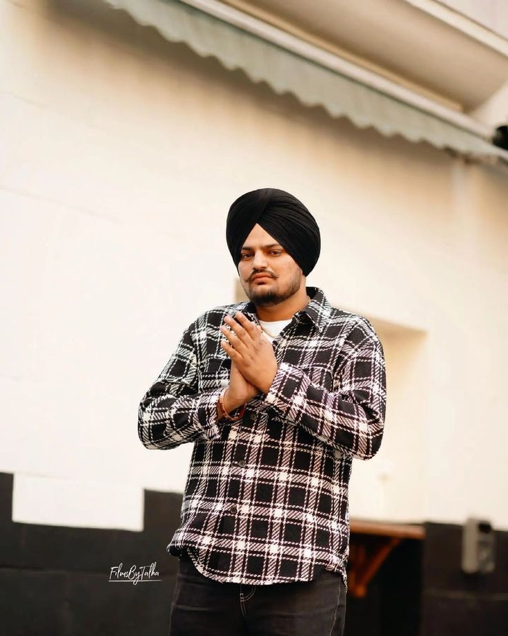 a man wearing a turban standing in front of a building holding a cell phone