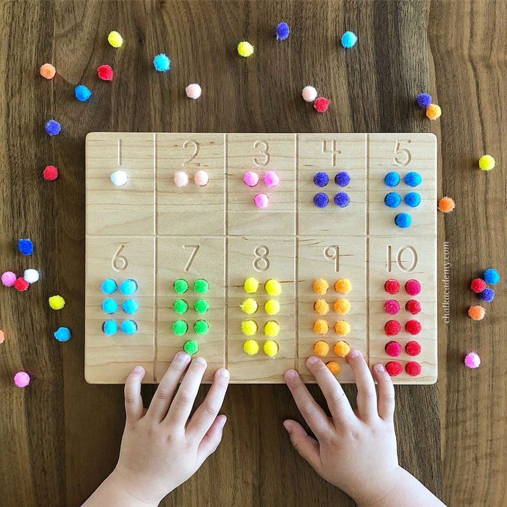 a child is playing with an abacusk game on the wooden table surrounded by colorful beads