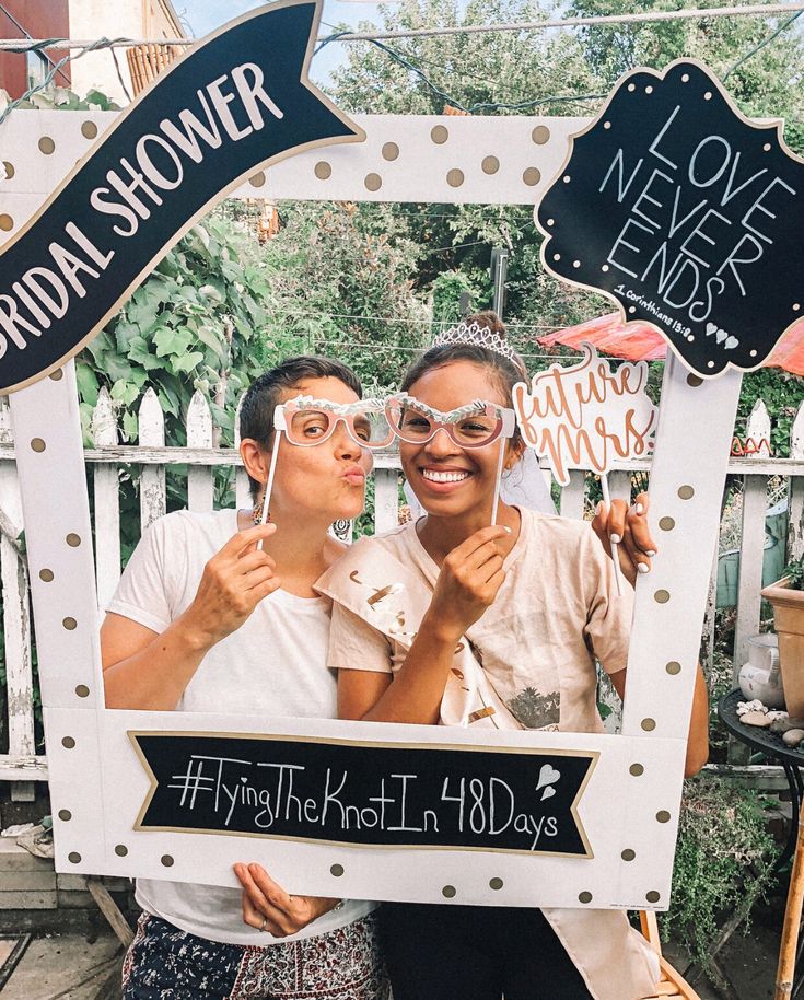 two women pose in front of a sign for bridal shower