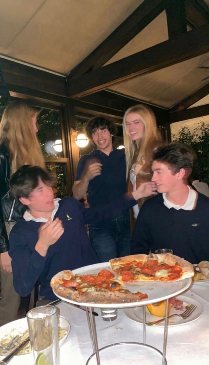 a group of people standing around a pizza on a table