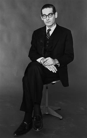 a black and white photo of a man in a suit sitting on a chair with his legs crossed