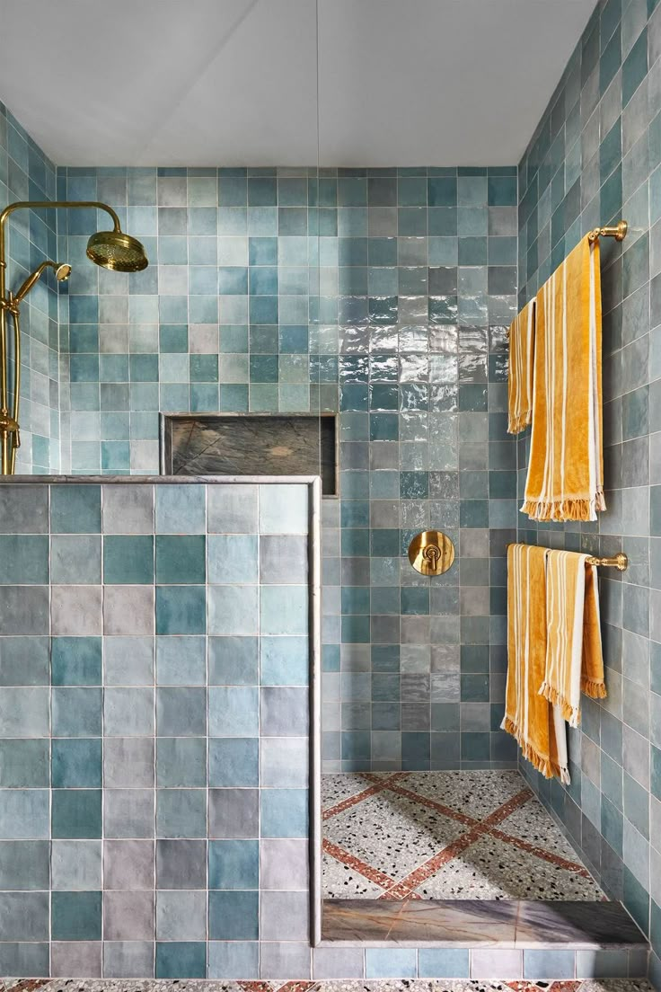 a blue tiled bathroom with gold fixtures and towels hanging on the shower head, along with two yellow hand towels