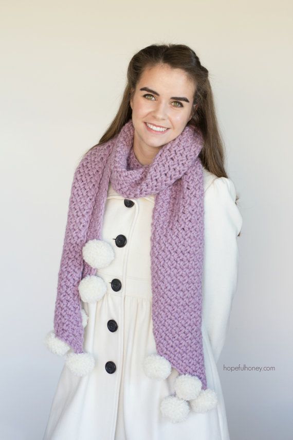 a woman wearing a purple scarf with pom - poms on the ends and a white coat over her shoulders