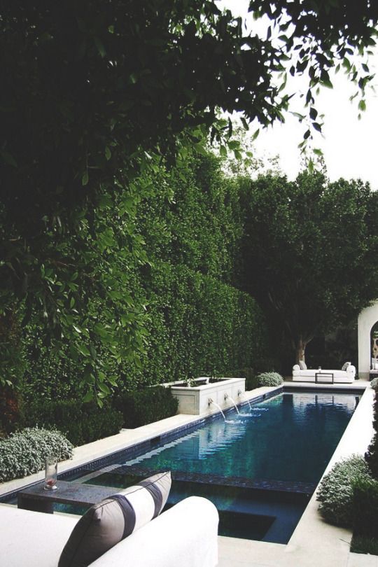 an outdoor swimming pool surrounded by greenery and white couches with pillows on it