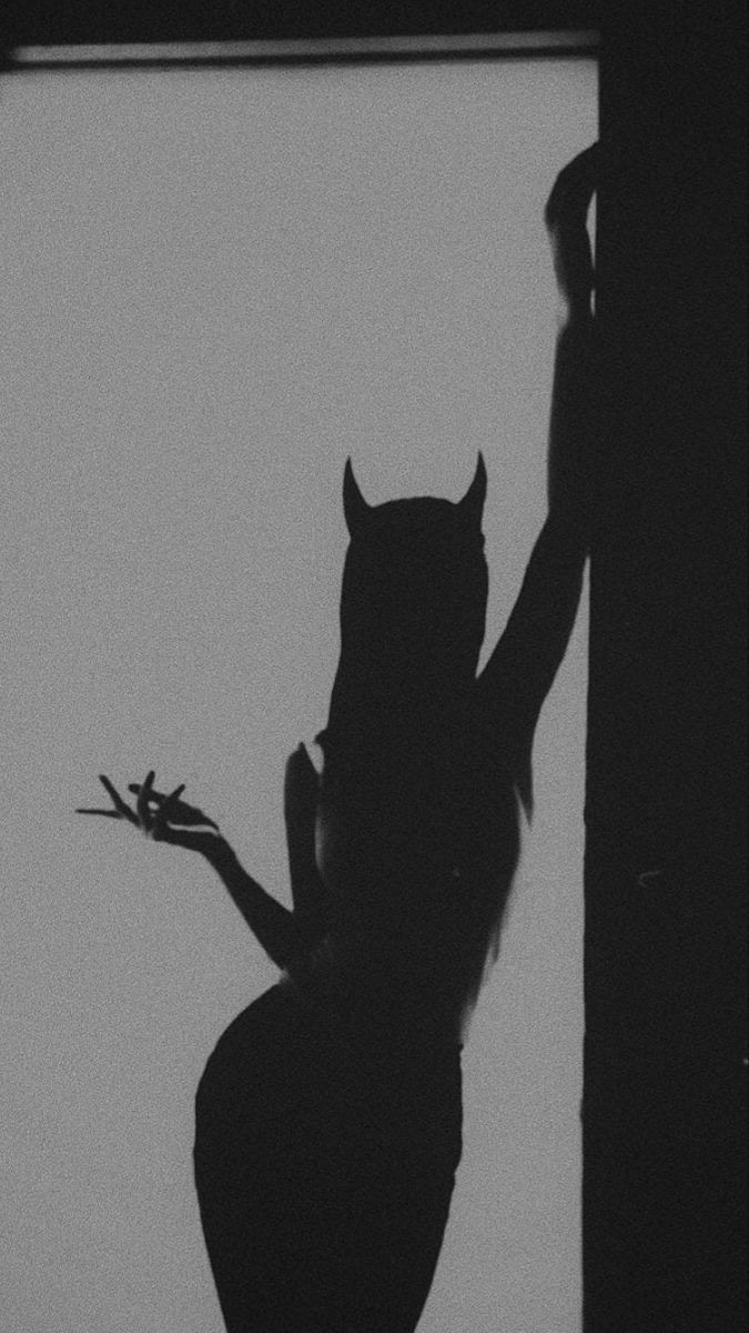 a black and white photo of a woman with an owl on her head, standing in front of a window