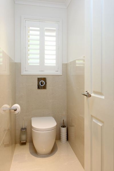 a white toilet sitting in a bathroom next to a window with shutters on it