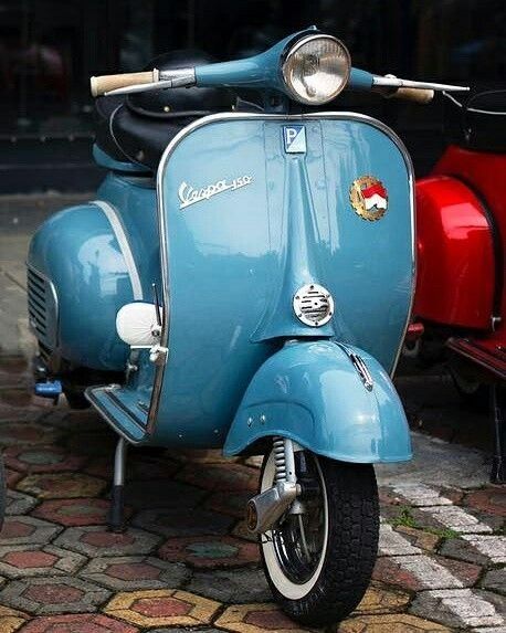 a blue scooter parked next to two red scooters on a cobblestone street