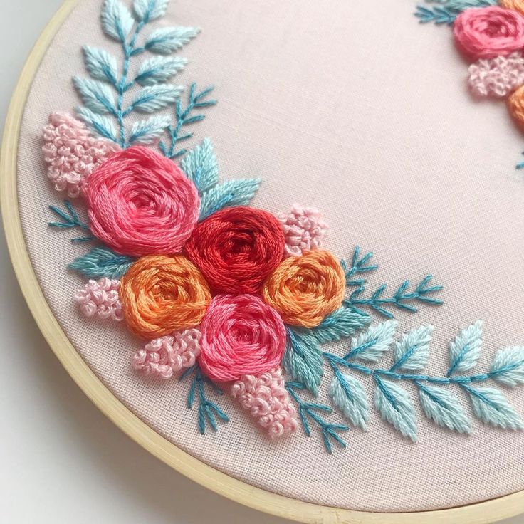 an embroidered hoop with flowers and leaves on the inside is shown in pink, orange, and blue