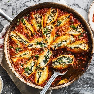 a pan filled with pasta and spinach on top of a marble table next to other dishes