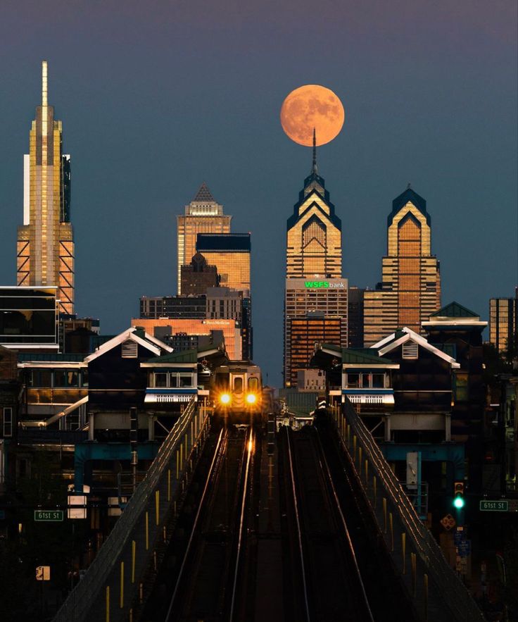 a full moon rises over the city skyline as a train goes down the tracks in front of it