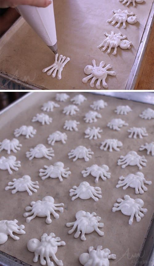 there are many small white crabs on the cookie sheet, and someone is decorating them with icing