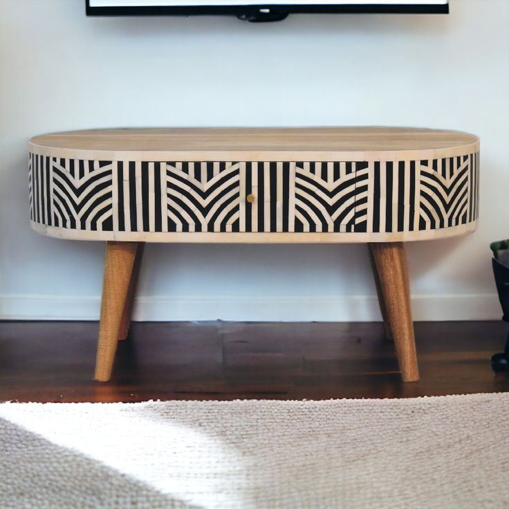 a tv mounted on the wall next to a wooden table with black and white designs