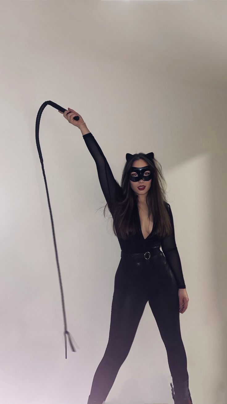 a woman in black catsuits and cat mask holding a whip with her right hand