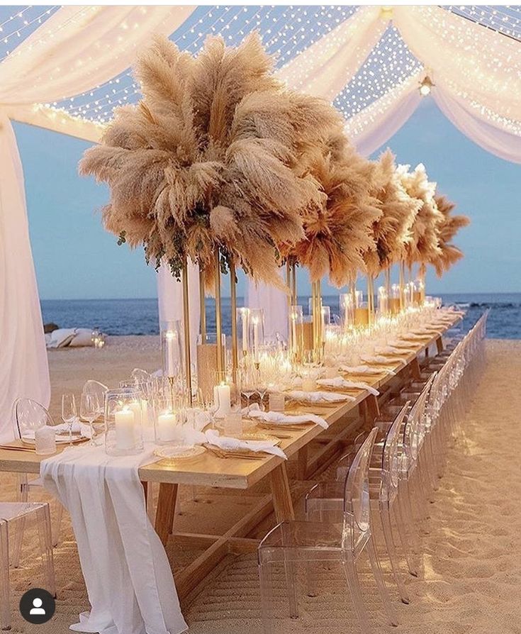 a long table set up on the beach with candles and flowers in tall vases