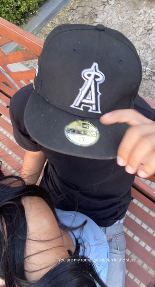 a man sitting on top of a wooden bench wearing a black hat and pointing at the camera