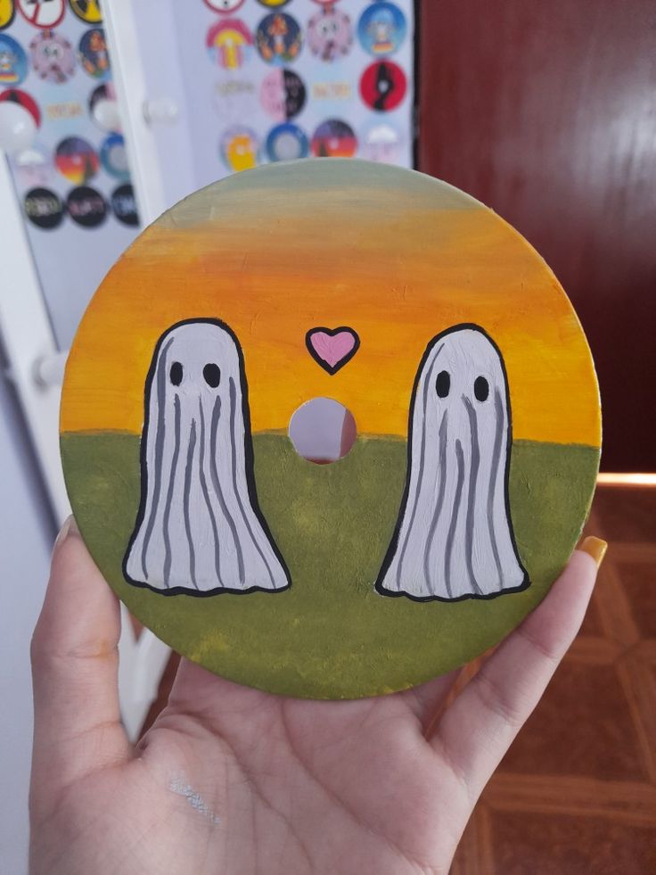 someone is holding up a painted disc with two ghost faces on it