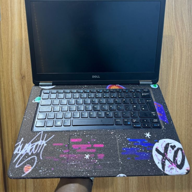 a laptop computer sitting on top of a wooden desk with graffiti all over the screen