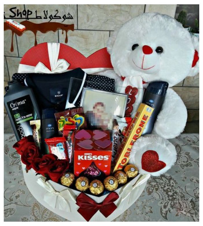 a white teddy bear sitting next to a valentine's day gift basket filled with chocolates and candy