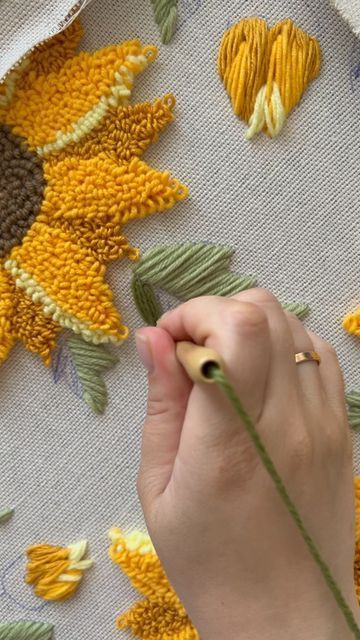 a woman is working on an embroidery project with sunflowers in the back ground