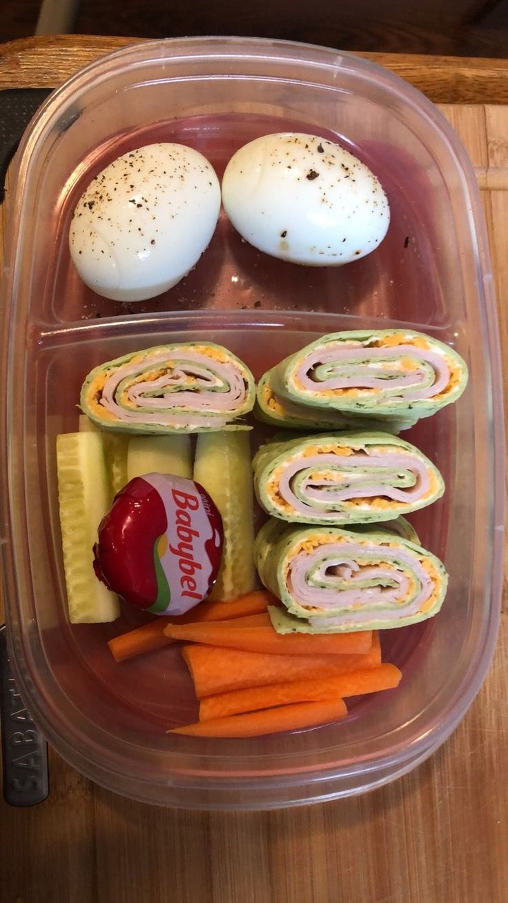 a plastic container filled with food on top of a wooden table next to an egg