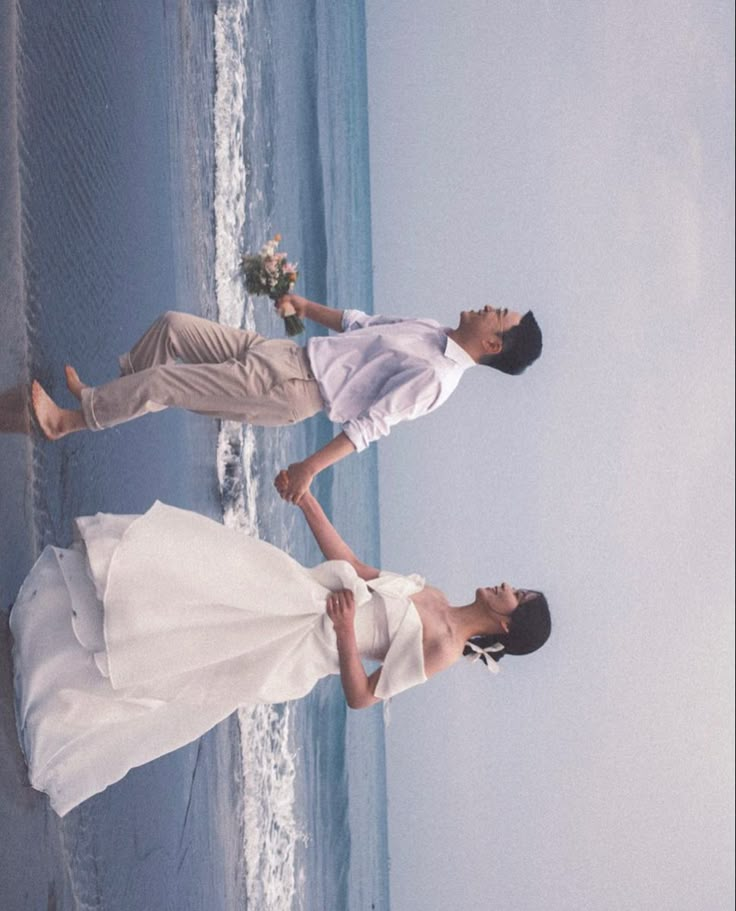 a man and woman standing next to each other in front of the ocean on their wedding day