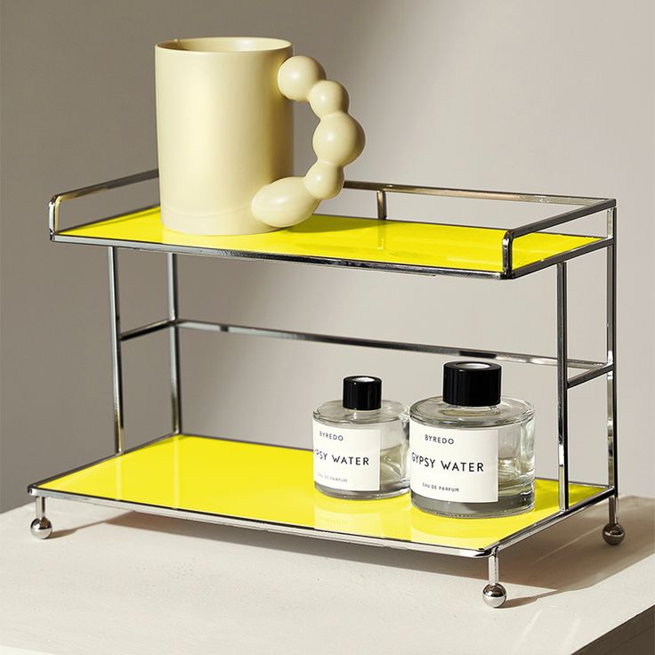 two bottles and a cup on a shelf with yellow shelves in the corner, next to each other