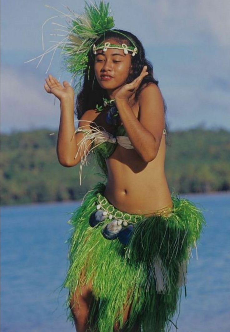 a woman in grass skirt standing on the beach