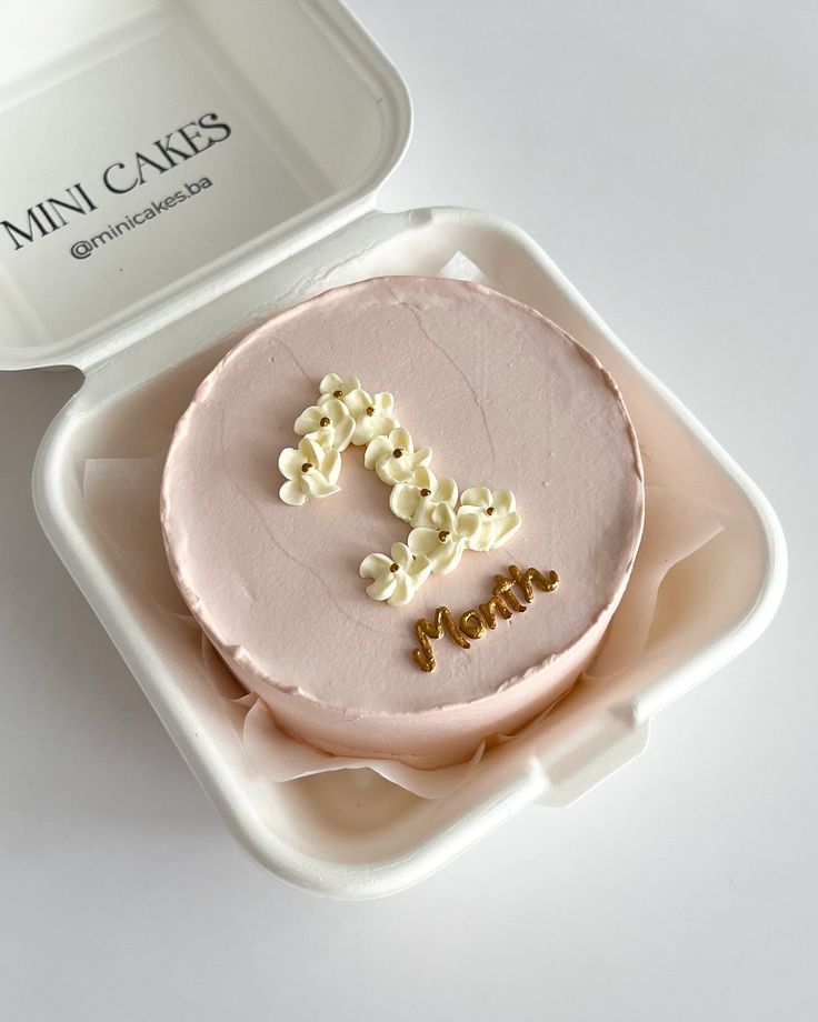 a pink frosted cake with the letter f on it in a plastic container next to a white tray