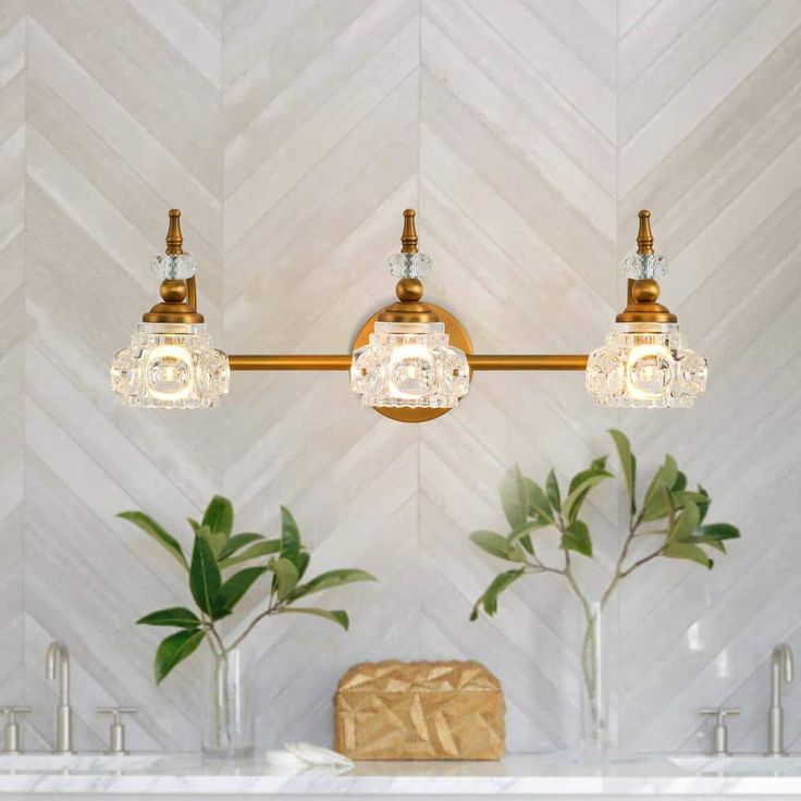 three lights are hanging on the wall above two sinks in a bathroom with marble counter tops