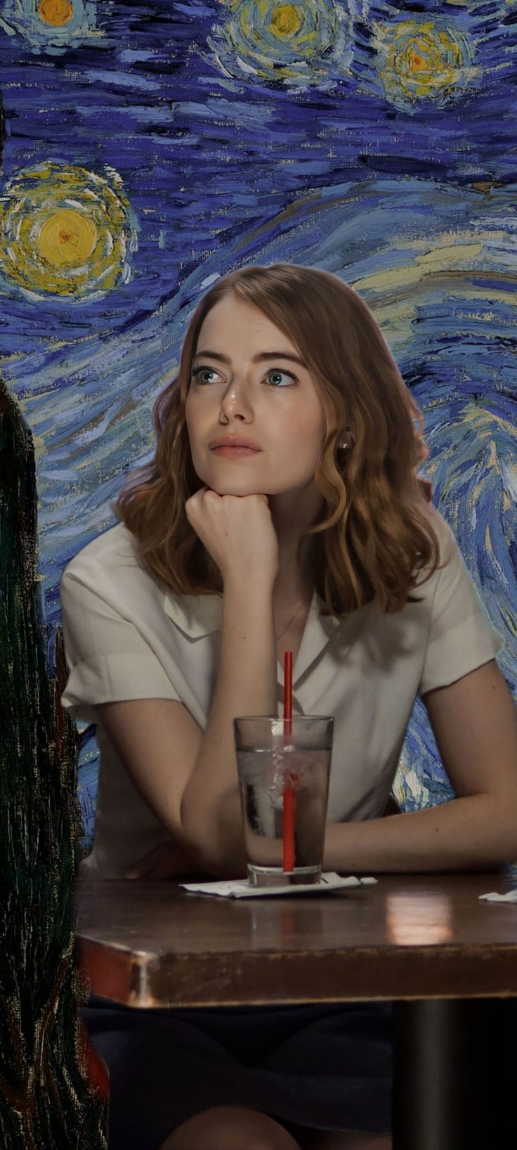 a woman sitting at a table with a drink in front of her and the painting behind her