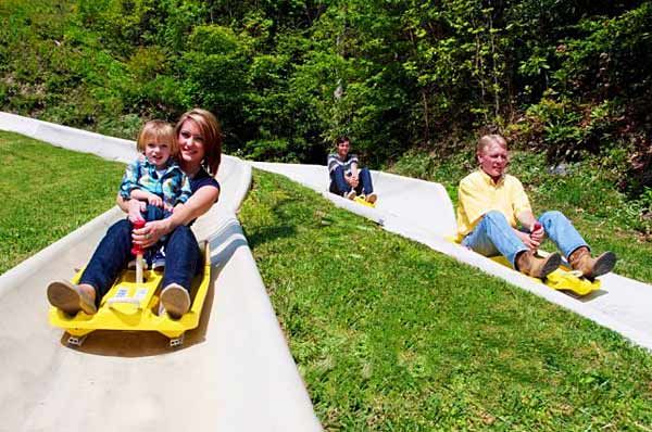 three adults and two children are riding down a hill on a yellow toy car with wheels