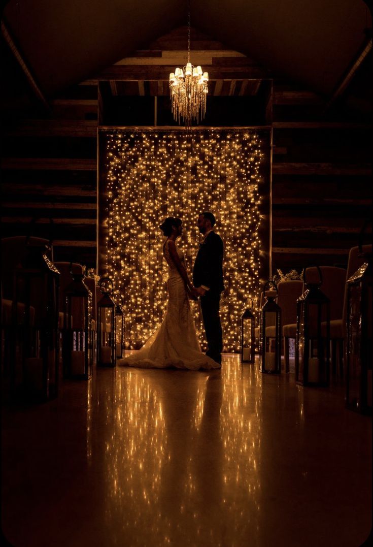 a bride and groom standing in front of a wall covered with lights at their wedding